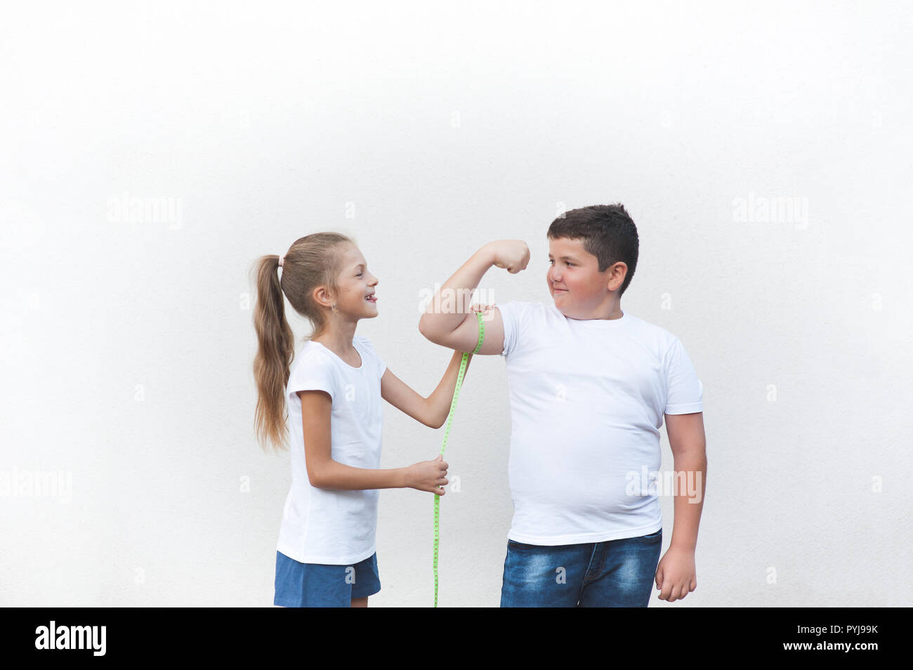 healthy slim little girl tease big fat boy measuring his muscle with tape copyspace Stock Photo