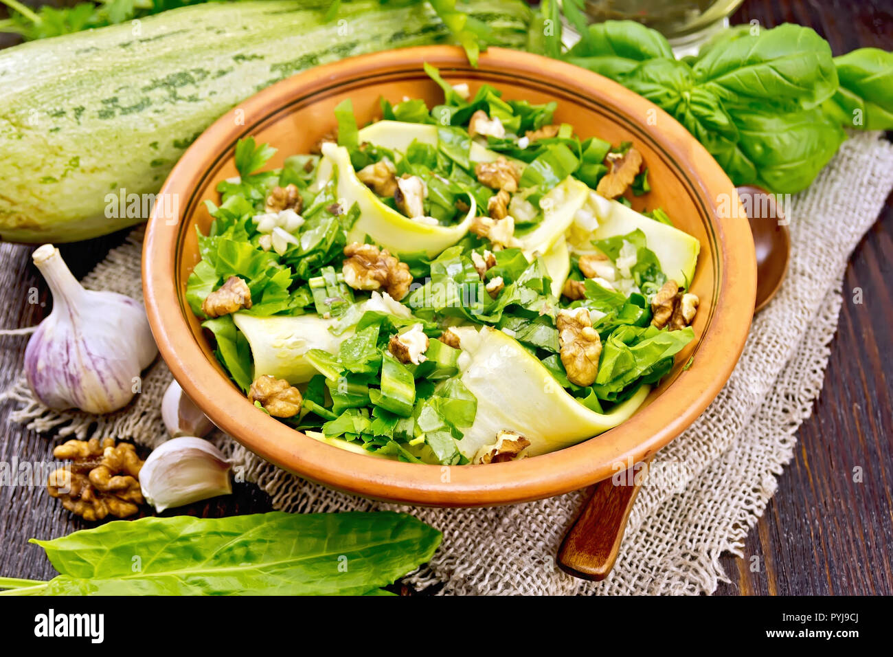 Salad of young zucchini, sorrel, garlic and nuts, seasoned with vegetable oil in a plate on napkin of sackcloth on a background of a dark wooden board Stock Photo