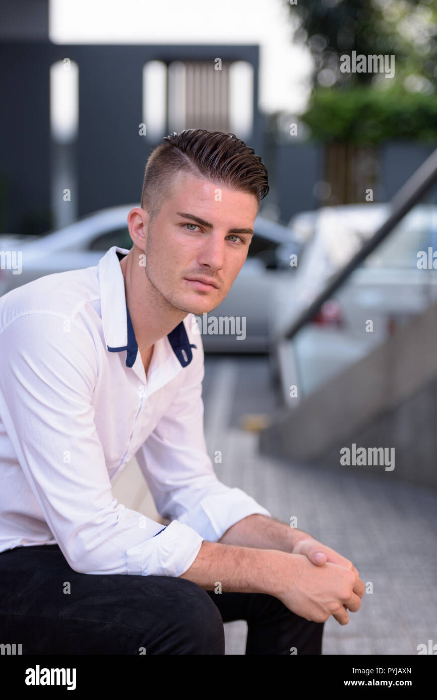 Young handsome man looking at camera while sitting outside moder Stock Photo