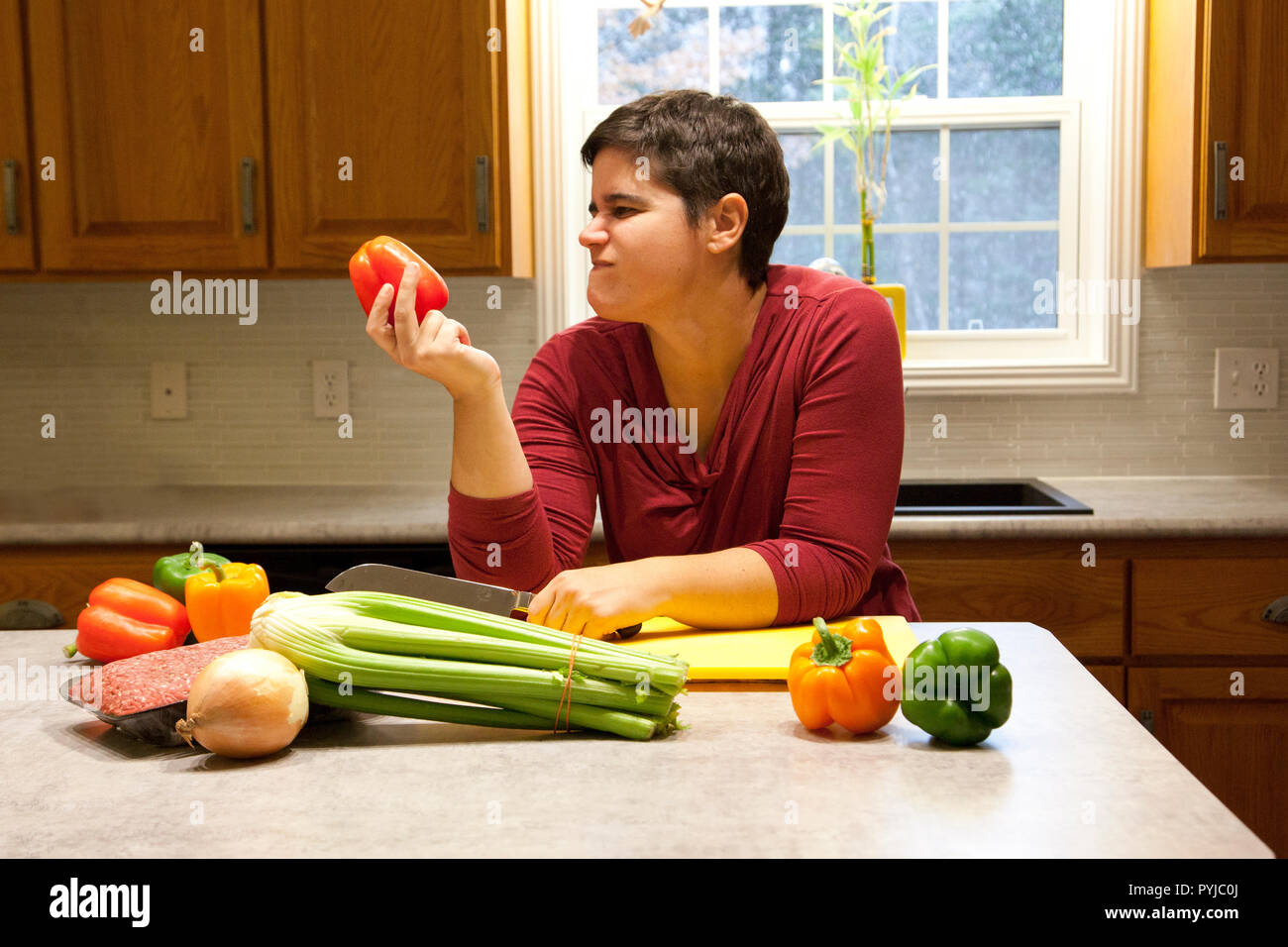 A woman holds a red bell pepper in her kitchen and makes an unhappy face Stock Photo