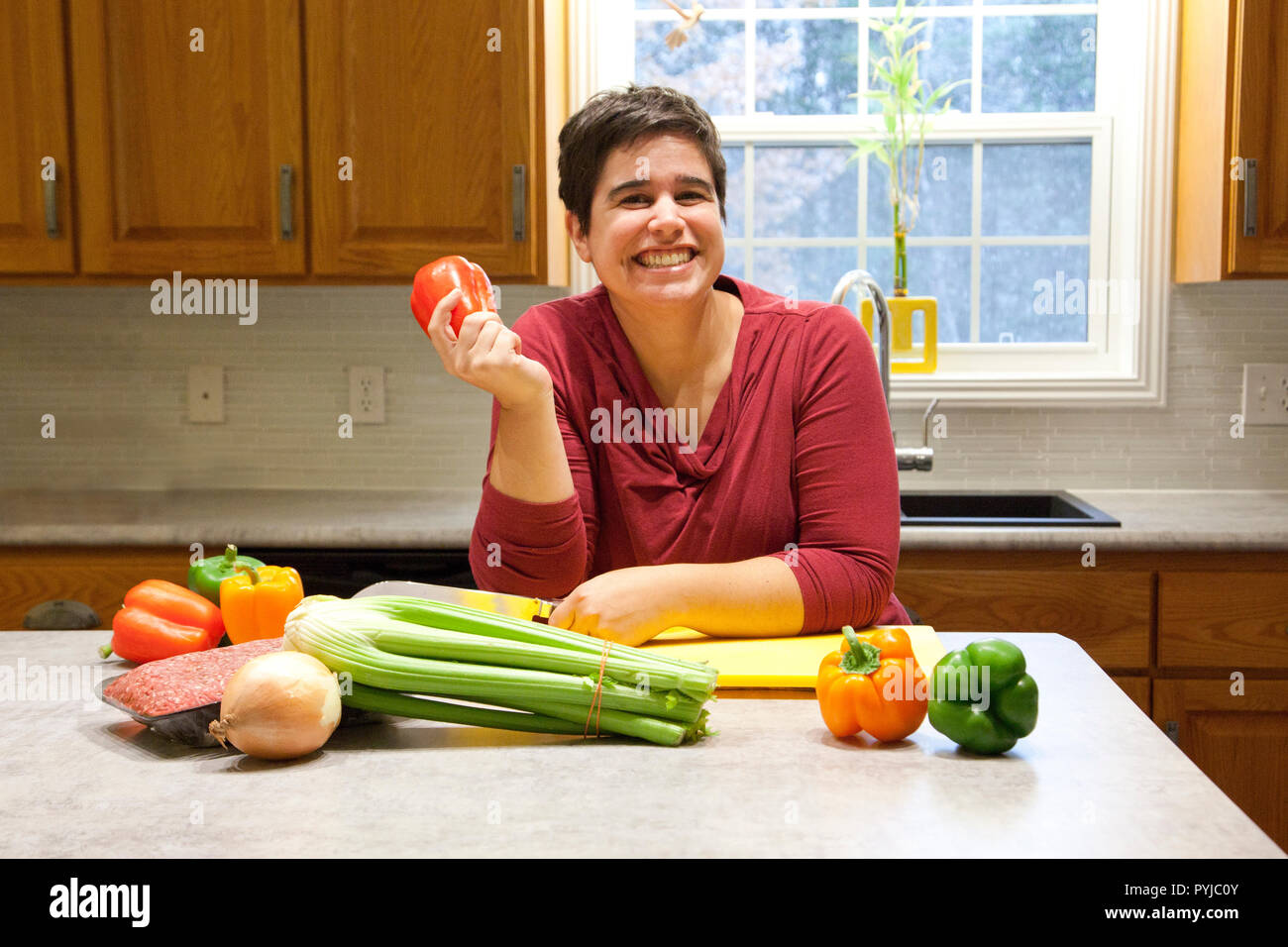 Holding a bell pepper and grinning in her beautiful kitchen, a woman prepares to cook healthy Stock Photo