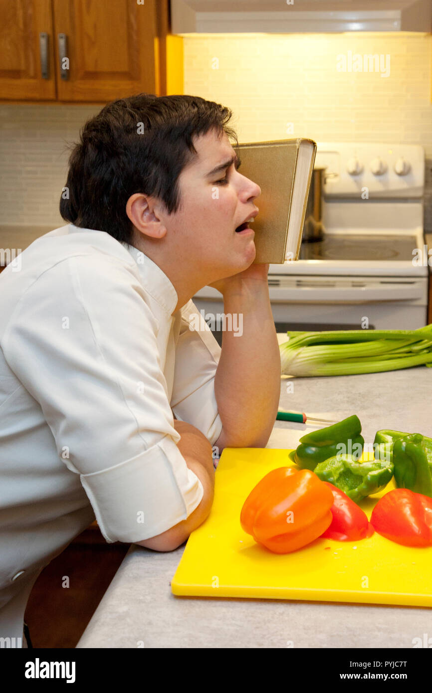 Vertical view of a chef whining or crying with vegetables and a cookbook in the kitchen Stock Photo