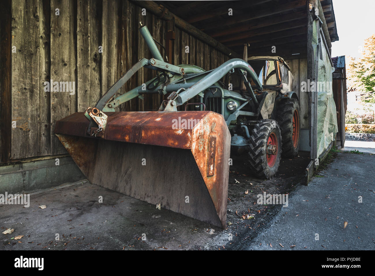 Old turquoise coloured Eicher tractor with lifting arm and rusty shovel in a dark wood shed, Bavaria, Germany Stock Photo