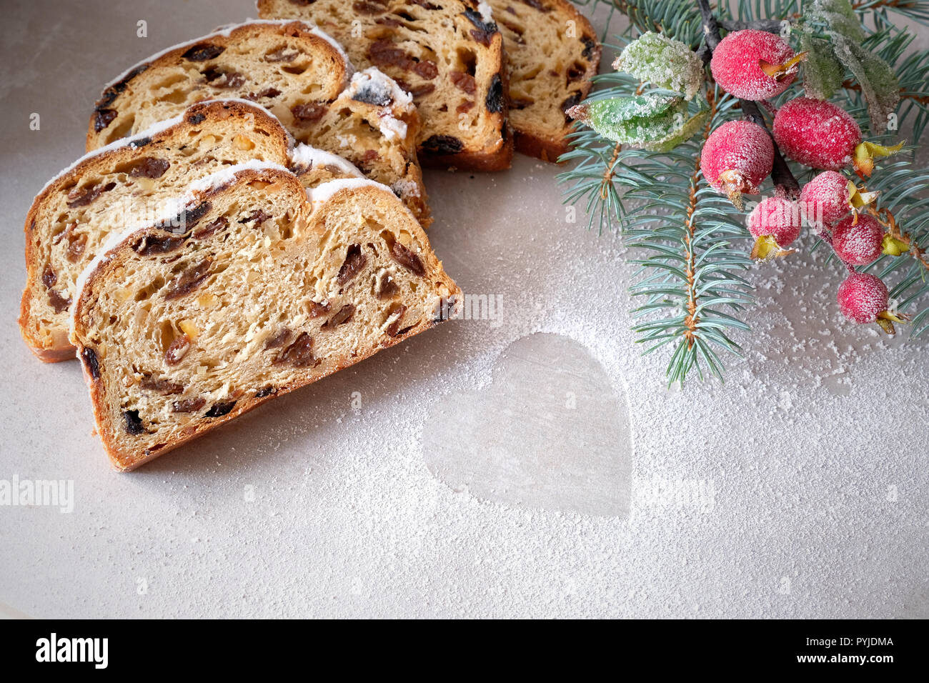 Christmas stollen on light stone board with fir twigs and frosted berriy decorations. Traditional German dessert for Christmas celebration. Stock Photo