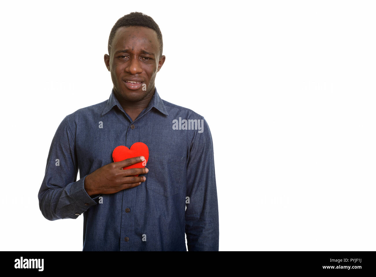Young sad African man holding red heart on chest  Stock Photo