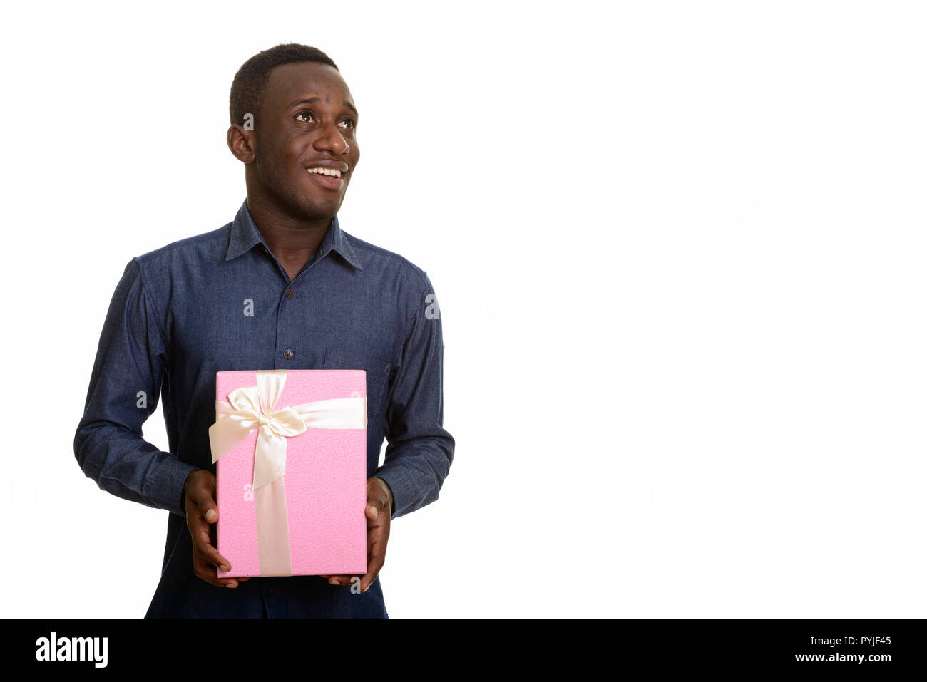 Happy African man smiling and holding gift box while thinking Stock Photo