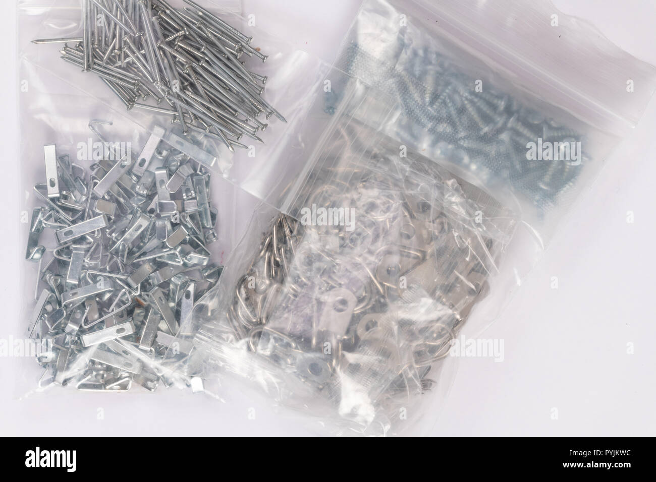 Groups of frame hanging metal plates, hooks, and nails isolated on white. frame hanging metal plates, hooks, nails, and screws in plastic packages iso Stock Photo