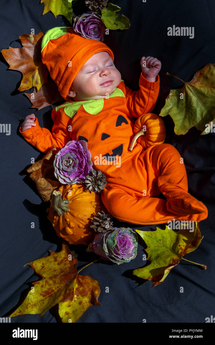 Surrey, UK, 28th October, 2018. A sleeping six week old male Caucasian baby boy, peacefully asleep, is dressed in an orange all-in-one babygrow with a Halloween theme pumpkin design, surrounded by pumpkins, gourds and fallen leaves appropriate to the autumnal occasion. Credit: Graham Prentice/Alamy Live News Stock Photo