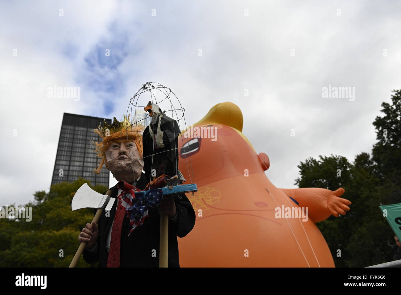 New York, U.S. 28 October 2018.  A man in a Trump mask stands before a 20-foot tall balloon depicting President Trump as a baby in diapers during a rally of protesters in Battery Park calling for the impeachment of Trump.  Protesters have used similar balloons in other anti-Trump protests in the U.S. and U.K.  The rally and march was organized by a group called By the People which accuses the president of committing high crimes and misdemeanors. Credit: Joseph Reid/Alamy Live News Stock Photo