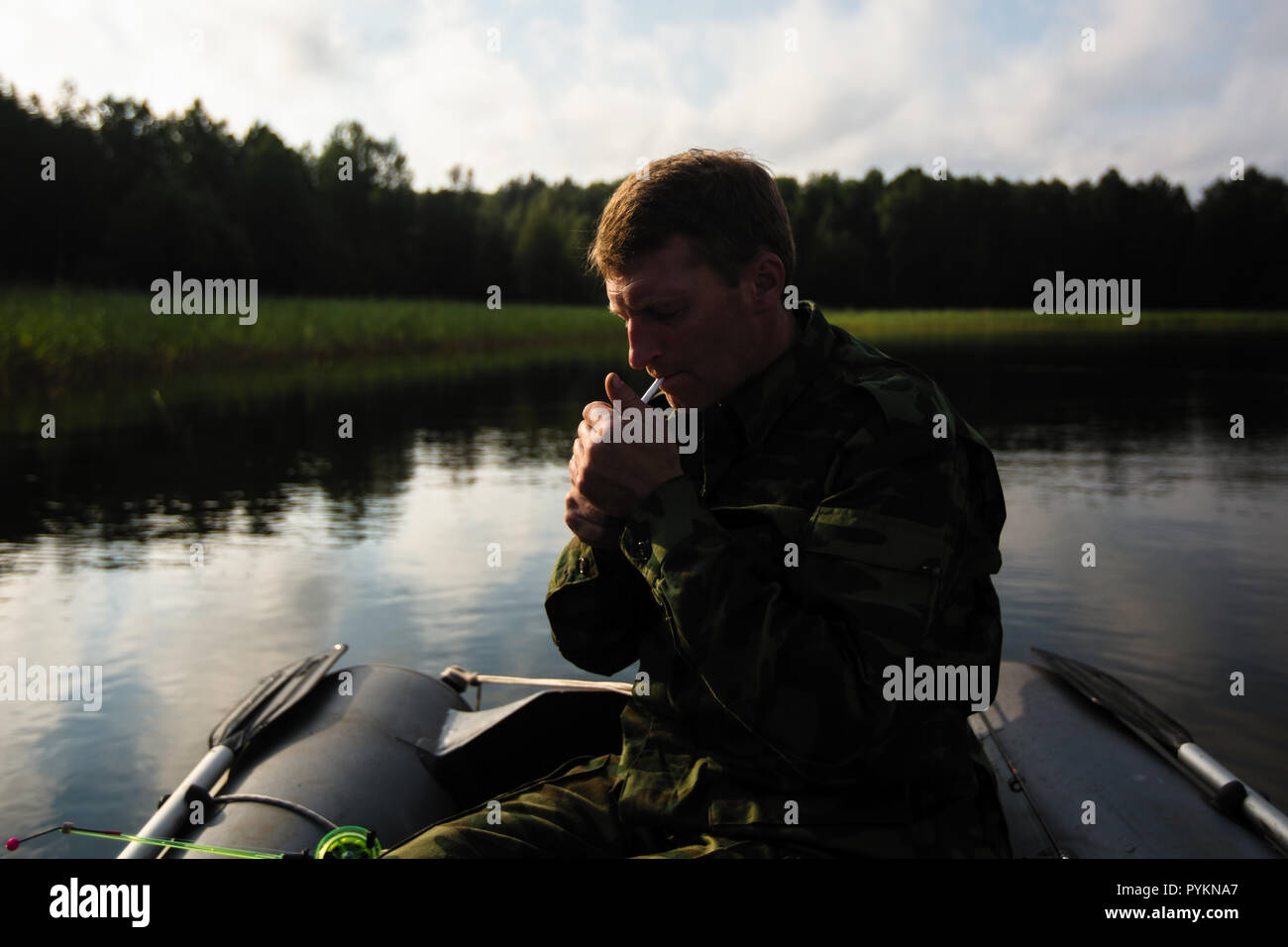 Man in an inflatable rubber boat on the lake lights a cigarette. Stock Photo