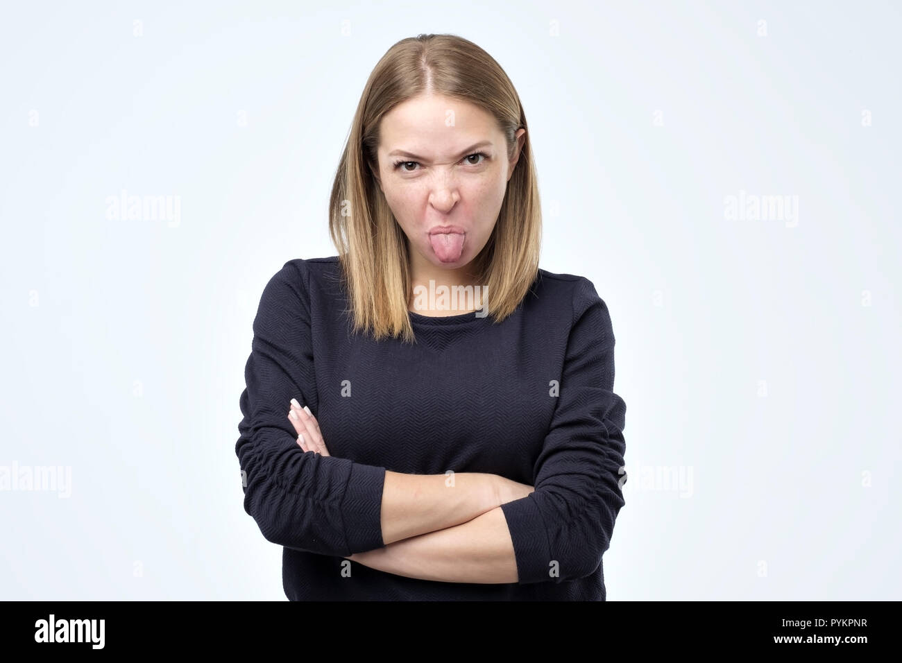 Dissatisfied woman frowns face, has disgusting expression, shows tongue, expresses disgust, irritated with somebody Stock Photo