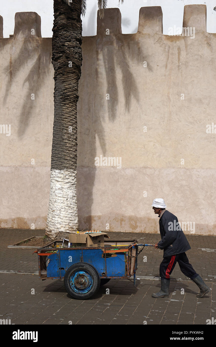 Man with wheel barrow walking along the city wall of Essaouira, Morocco Stock Photo