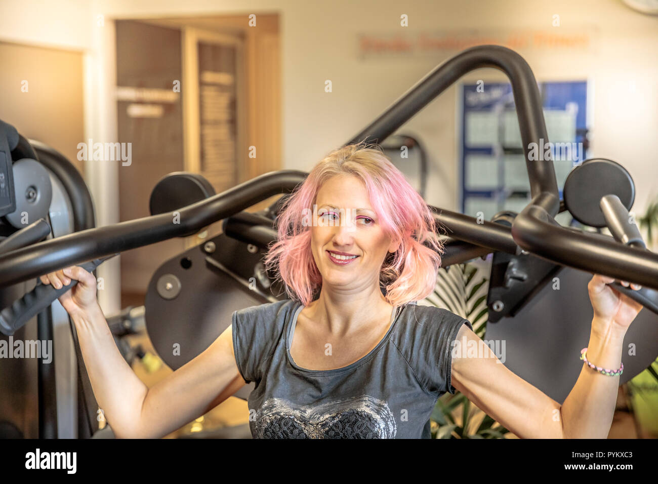 Portrait of fitness female athlete working on seated shoulder press machine. Training arms triceps biceps muscles in modern gym. Healthy lifestyle concept. Stock Photo