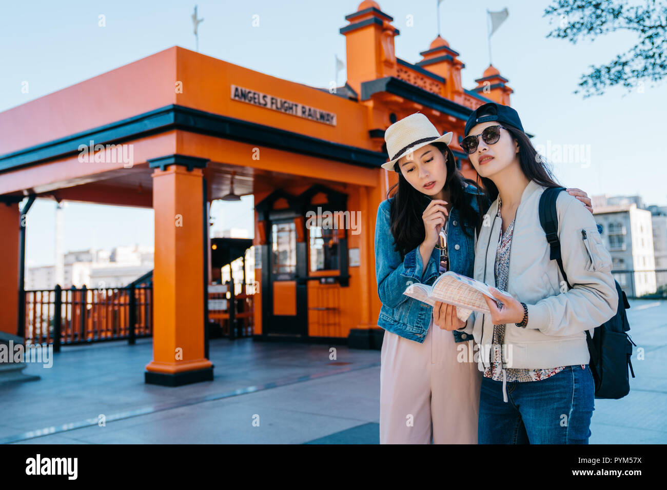 two female travelers standing in front of the Angels flight railway station and reading at the guidebook. Friends two girls having fun vacation trip.  Stock Photo