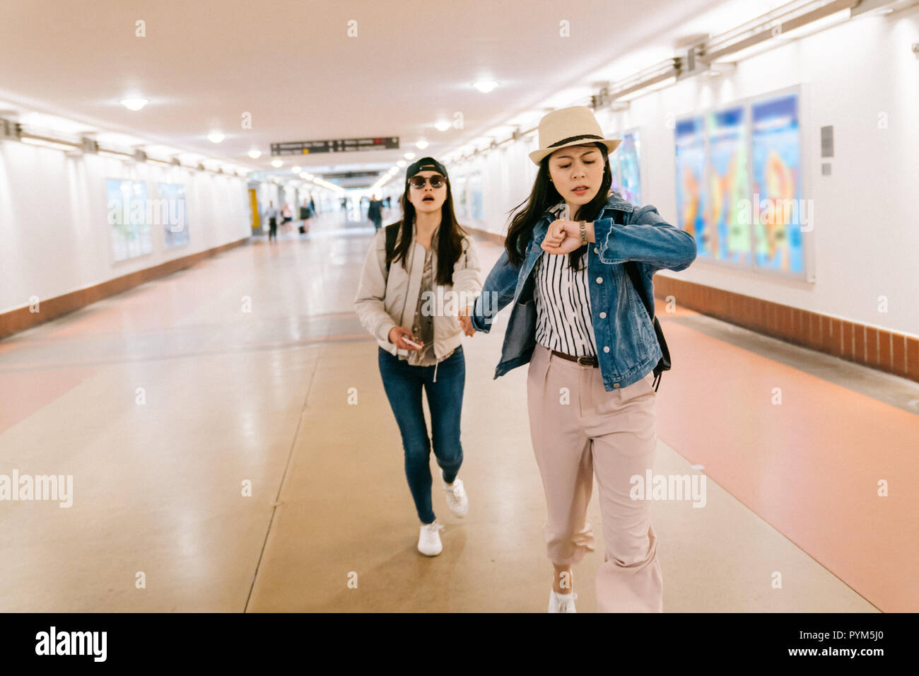 asian sisters are in a rush to catch the train. female travelers running in the passageway in the railway station. backpacker self-guided trip in USA  Stock Photo