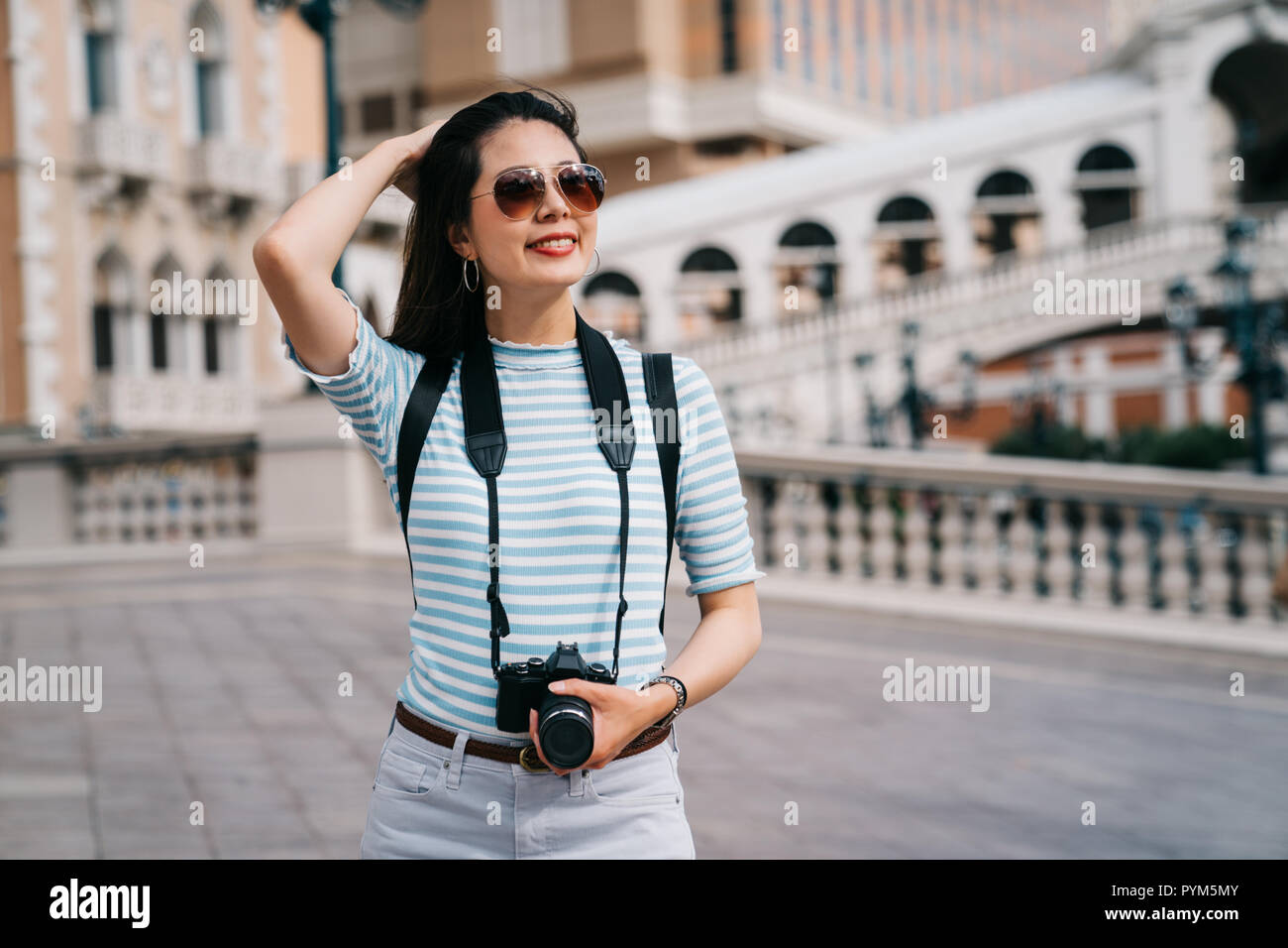 wind blowing the beautiful traveler's long hair while she joyfully walking on the bridge. Japanese lady tourist having holiday in America. Asian woman Stock Photo