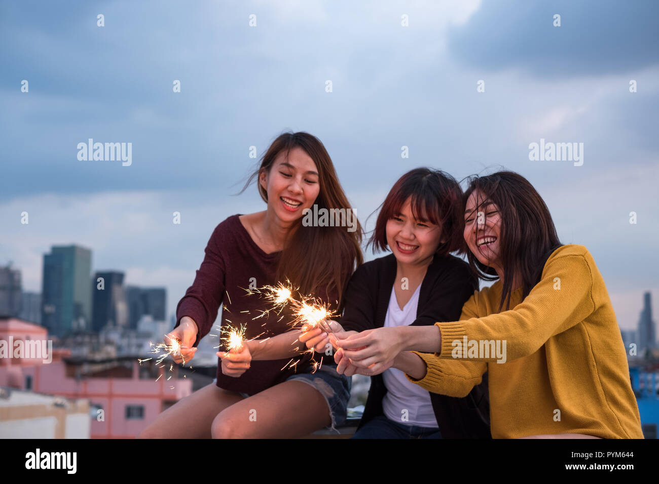 Happy group of asian girl friends enjoy and play sparkler at roof top party at evening sunset,Holiday celebration festive,teenage lifestyle,freedom an Stock Photo