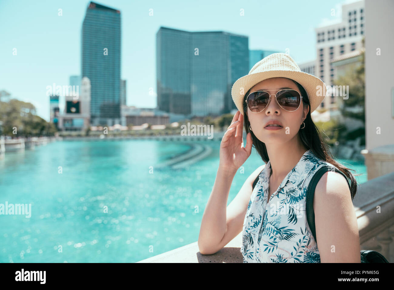 asian girl with hat and sunglasses standing on the balcony in las vegas travel in holiday. clean blue water in the big pond in city center in vegas. s Stock Photo
