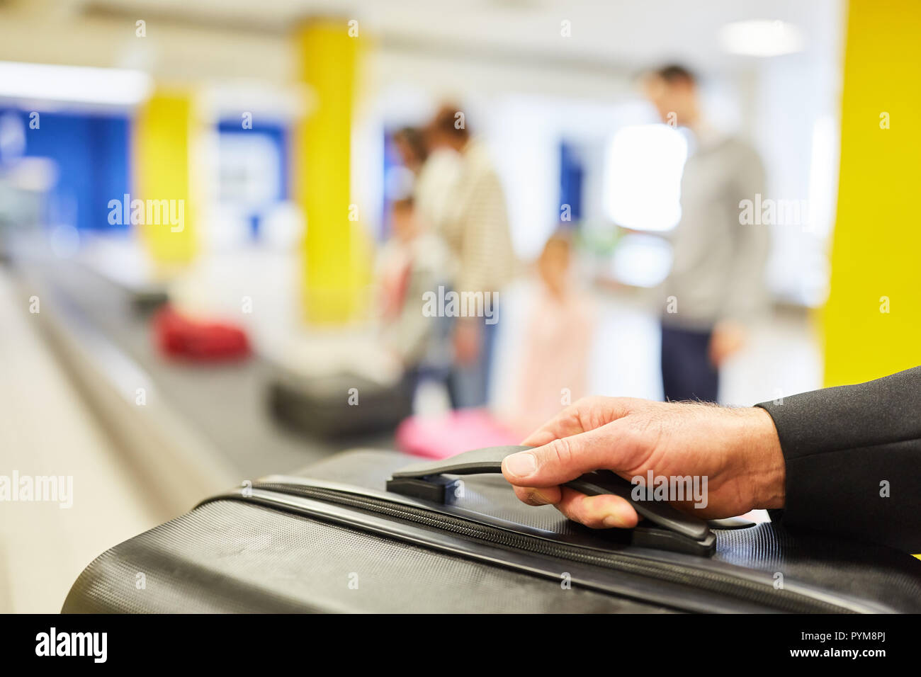Hand of a traveler holding a suitcase while picking up from the luggage belt in the airport terminal Stock Photo
