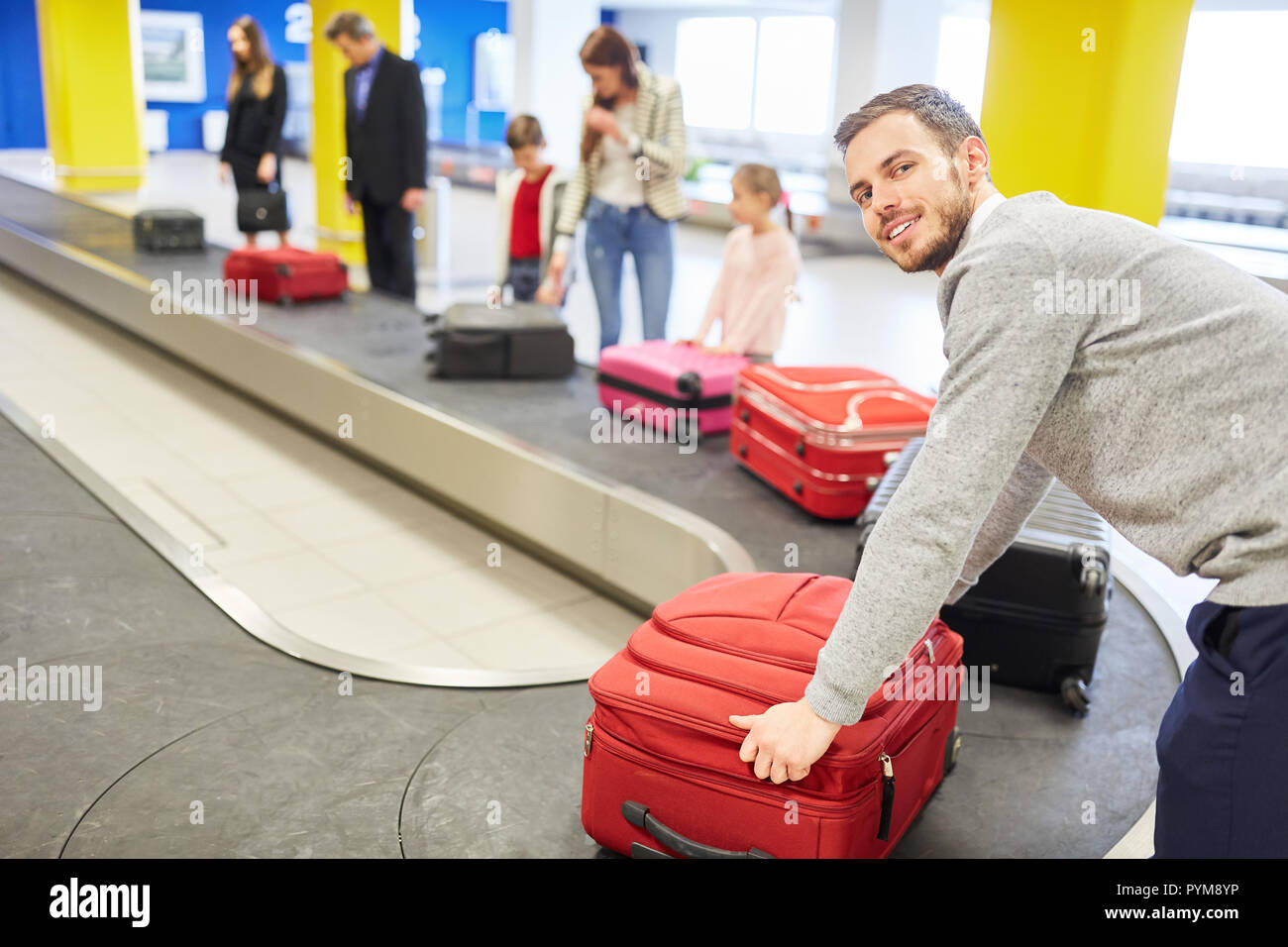 Family and other travelers on the luggage belt pick up their bags after the trip arrives Stock Photo
