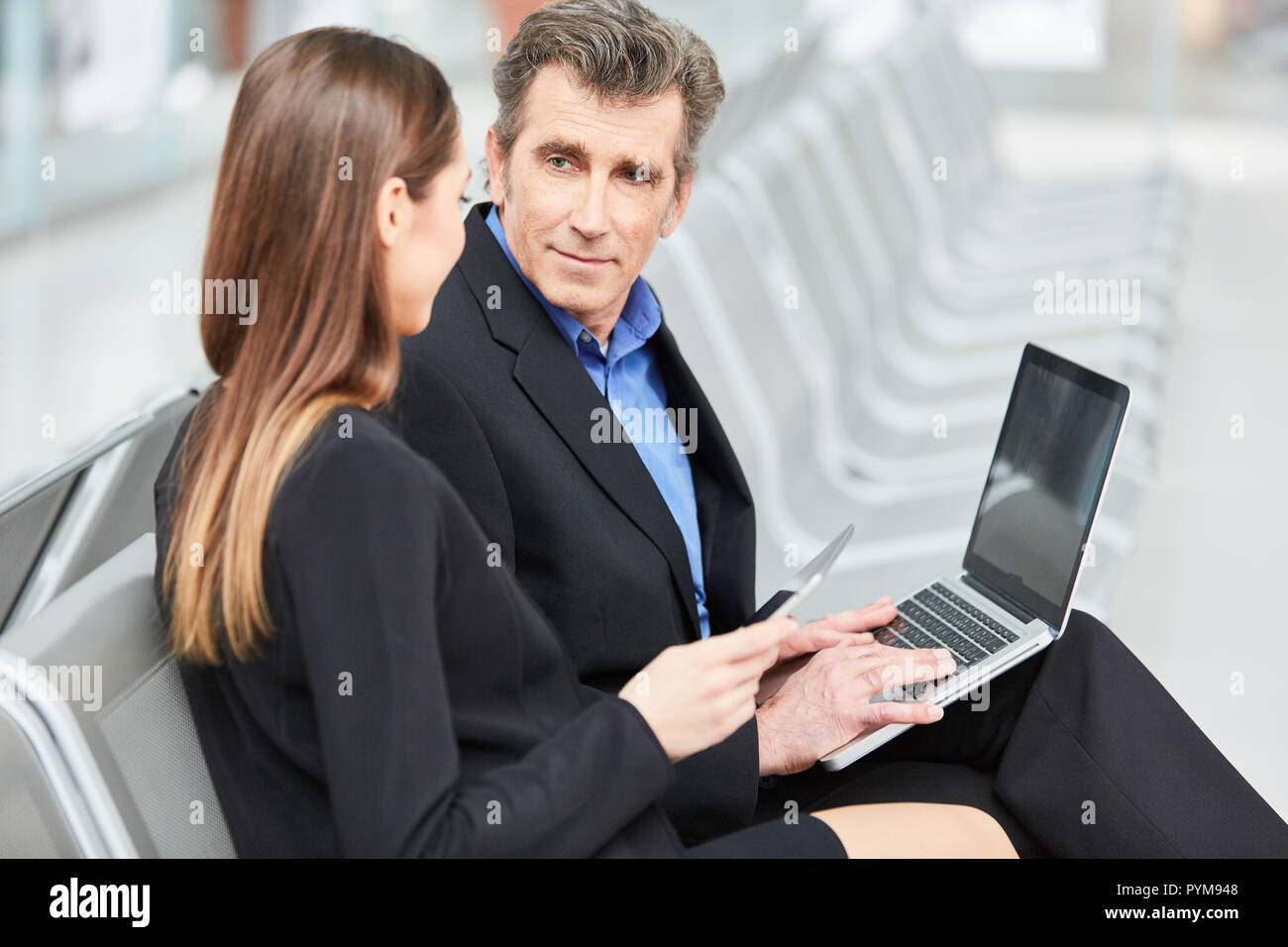Two business people with laptop computer before business trip in airport terminal Stock Photo