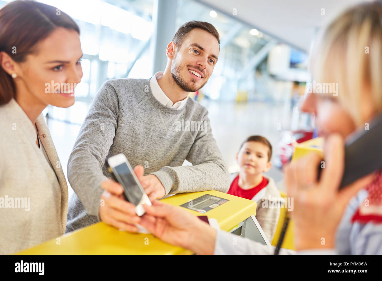 Family with smartphone at the check-in desk in the airport terminal waiting for the boarding pass Stock Photo