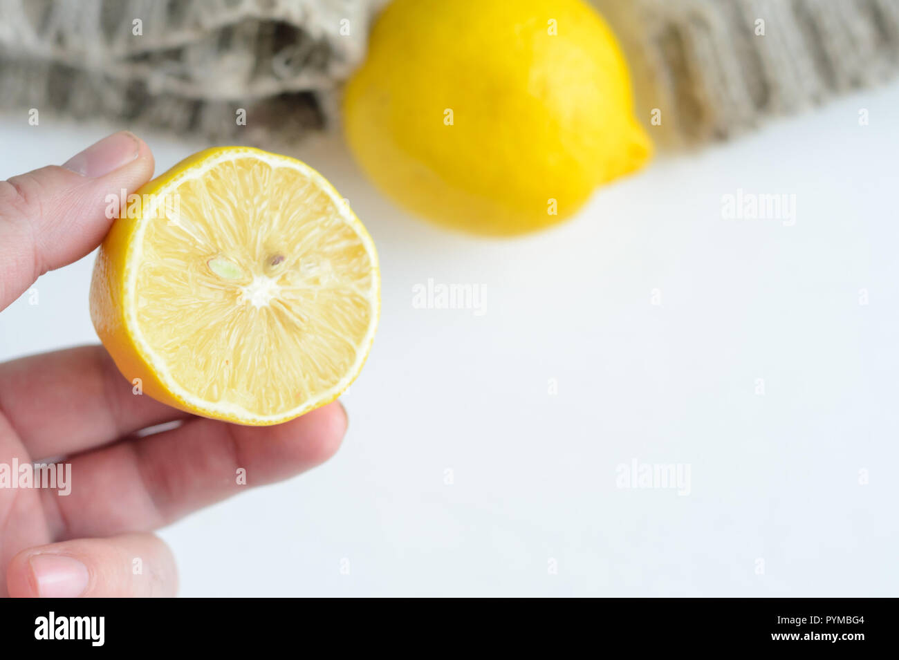 Hand holds half of lemon on a white wooden background. Stock Photo