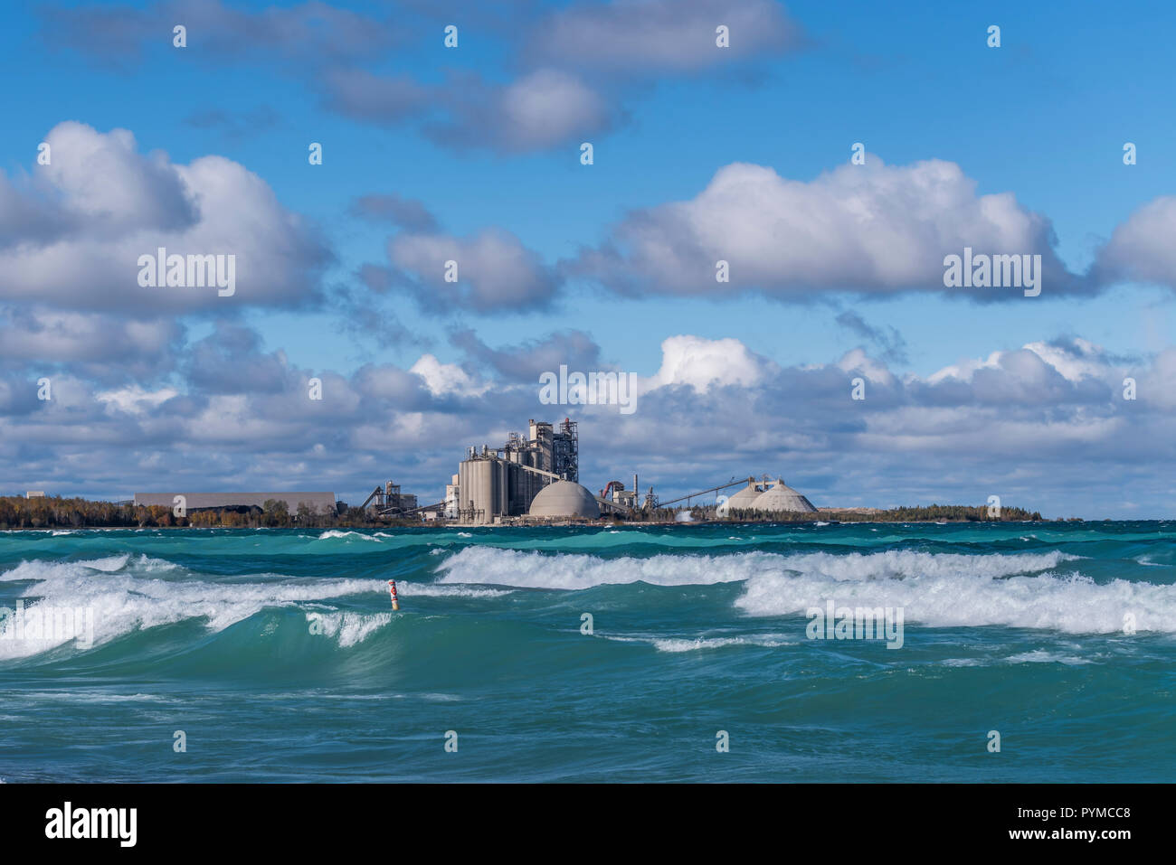 An industrial plant (Cement Plant) on the shore of a lake, from across the water with breaking waves in the foreground. Stock Photo