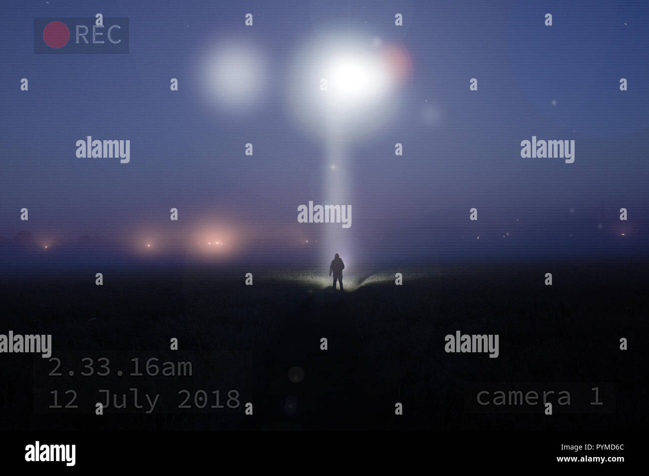A picture at night as a UFO shines down on a silhouette of a lonely figure standing in a misty field. With the image captured on cctv Stock Photo