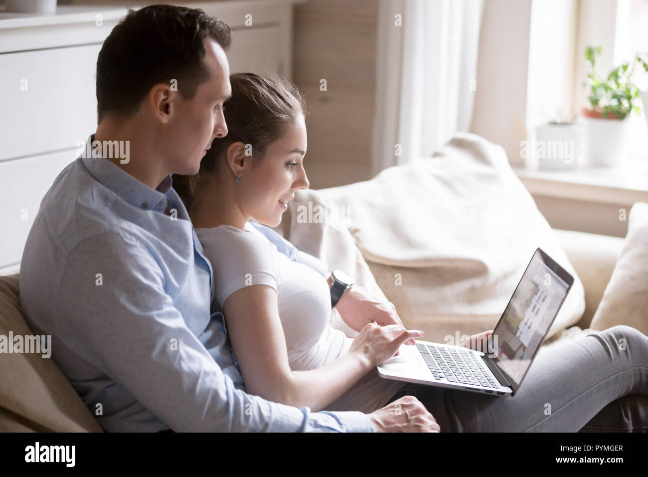 Millennial couple sitting on couch using laptop Stock Photo
