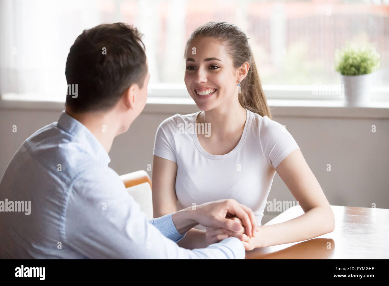 Happy spouses talking holding hands sitting in the kitchen Stock Photo