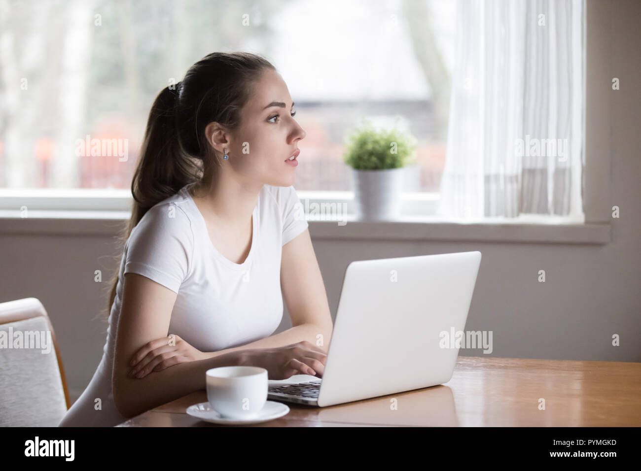 Serious pensive woman using laptop sitting in the kitchen Stock Photo