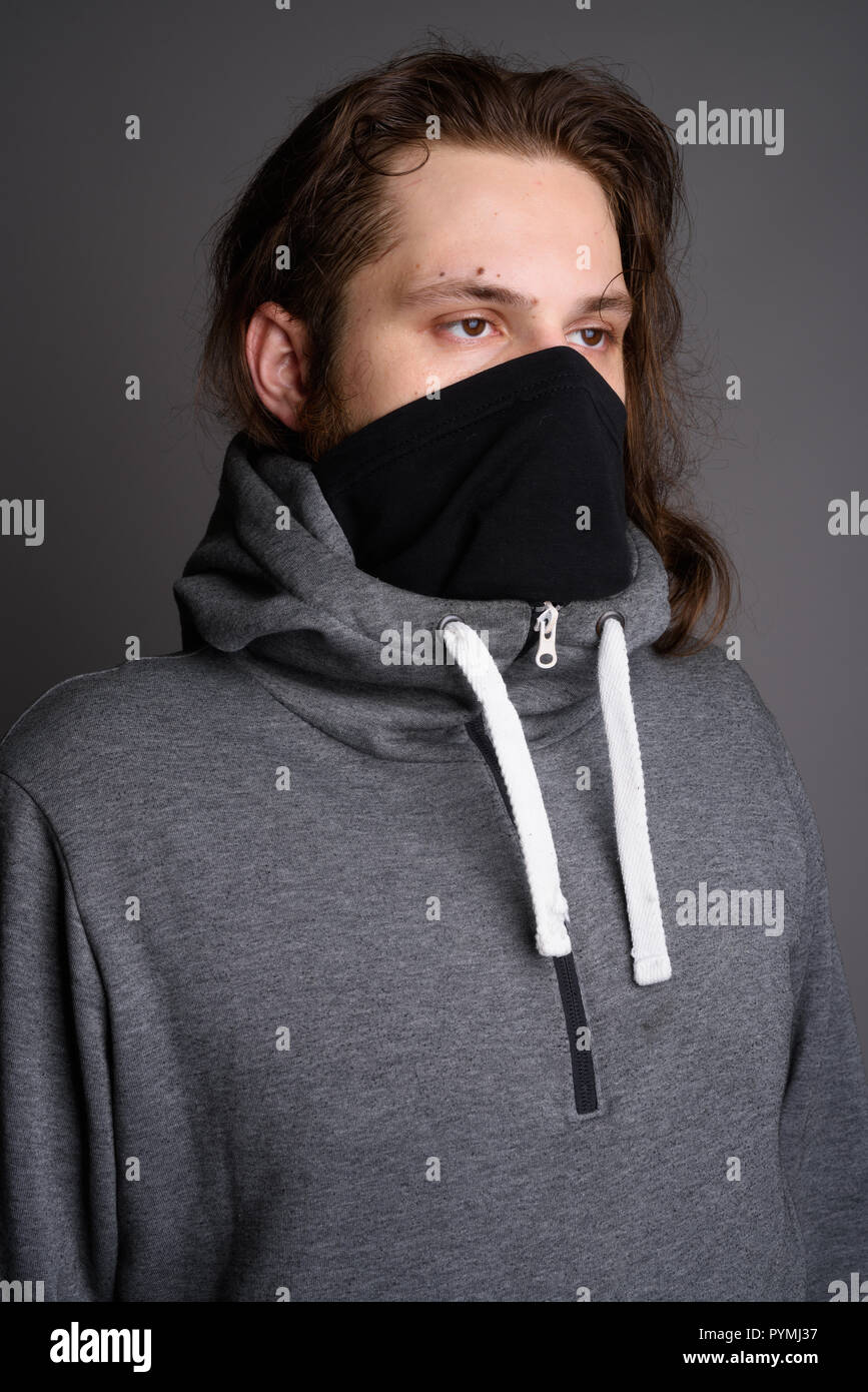 Young bearded man wearing gray hoodie and mask against gray back Stock Photo