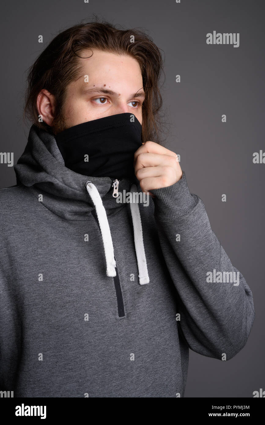 Young bearded man wearing gray hoodie and mask against gray back Stock Photo