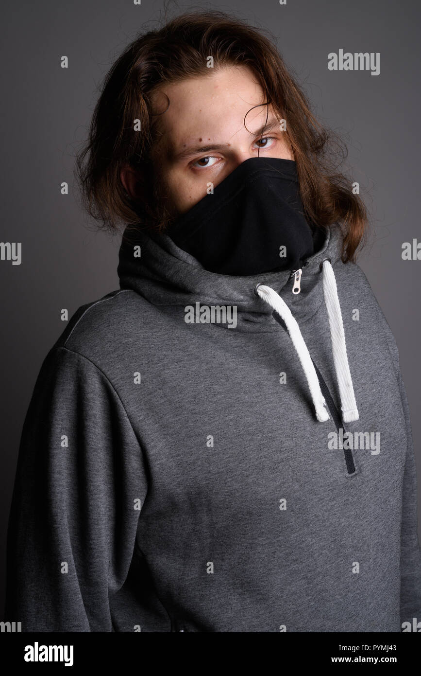 Young bearded man wearing gray hoodie and mask against gray back Stock Photo