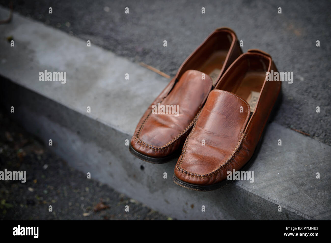 Shiny brown leather shoes left out on the concrete pavement Stock