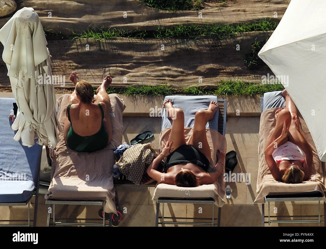 Three women sunbathe by a swimming pool in a hotel in Aqaba, Jordan Stock Photo