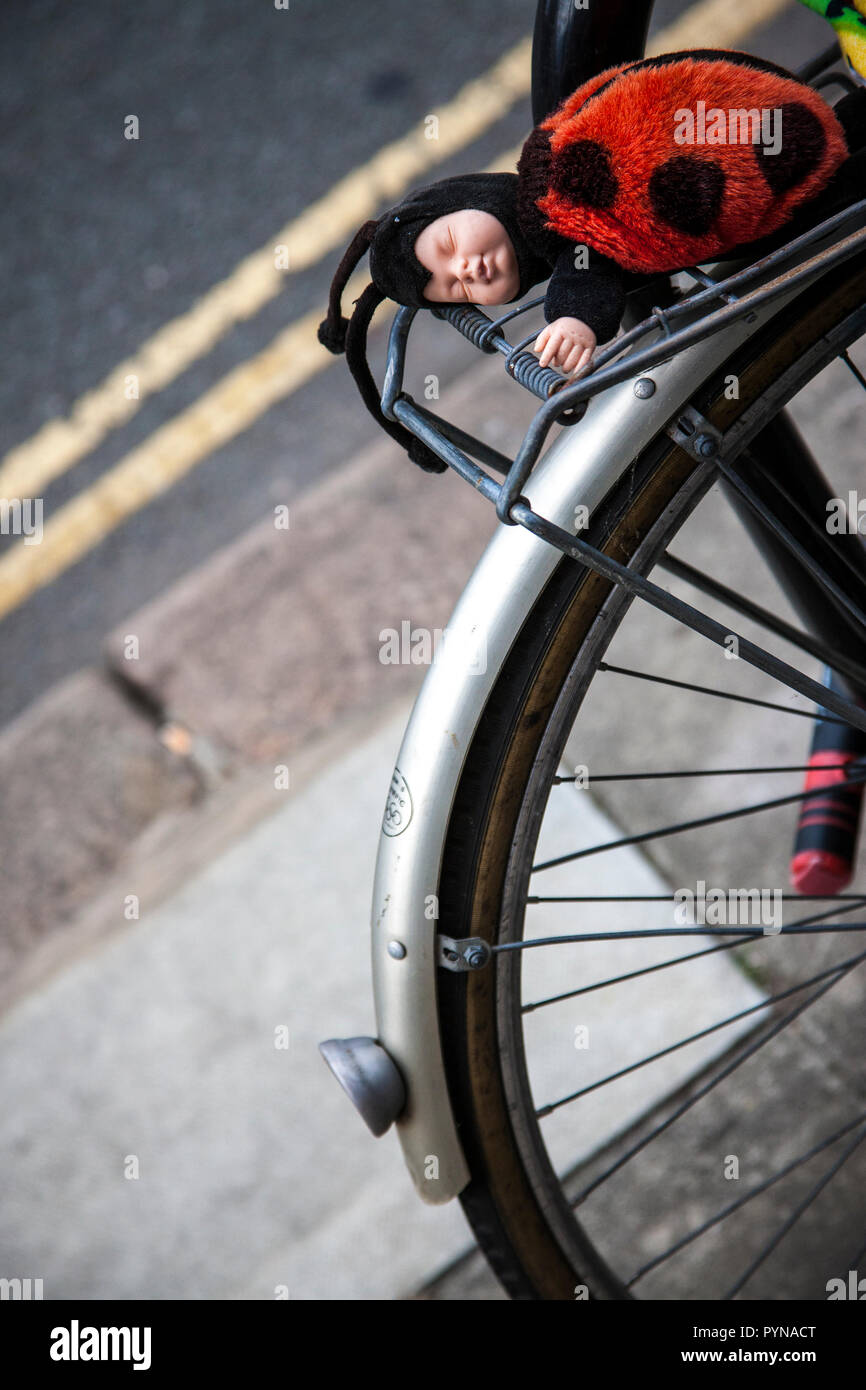 ANNE GEDDES LADYBUG BABY LADYBIRD DOLL on bicycle colour on greyluggage snap on back wheel Stock Photo