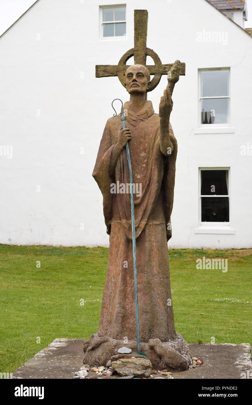 Statue of St Aidan first bishop of Lindisfarne monastery with white Manor House Hotel on Holy Island at the Priory ruins England UK Stock Photo