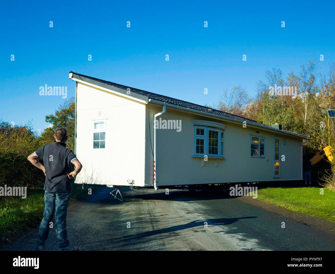 A prefabricated section of a static home building stuck in a narrow site entrance and being manoeuvered into place by a gang of men Stock Photo