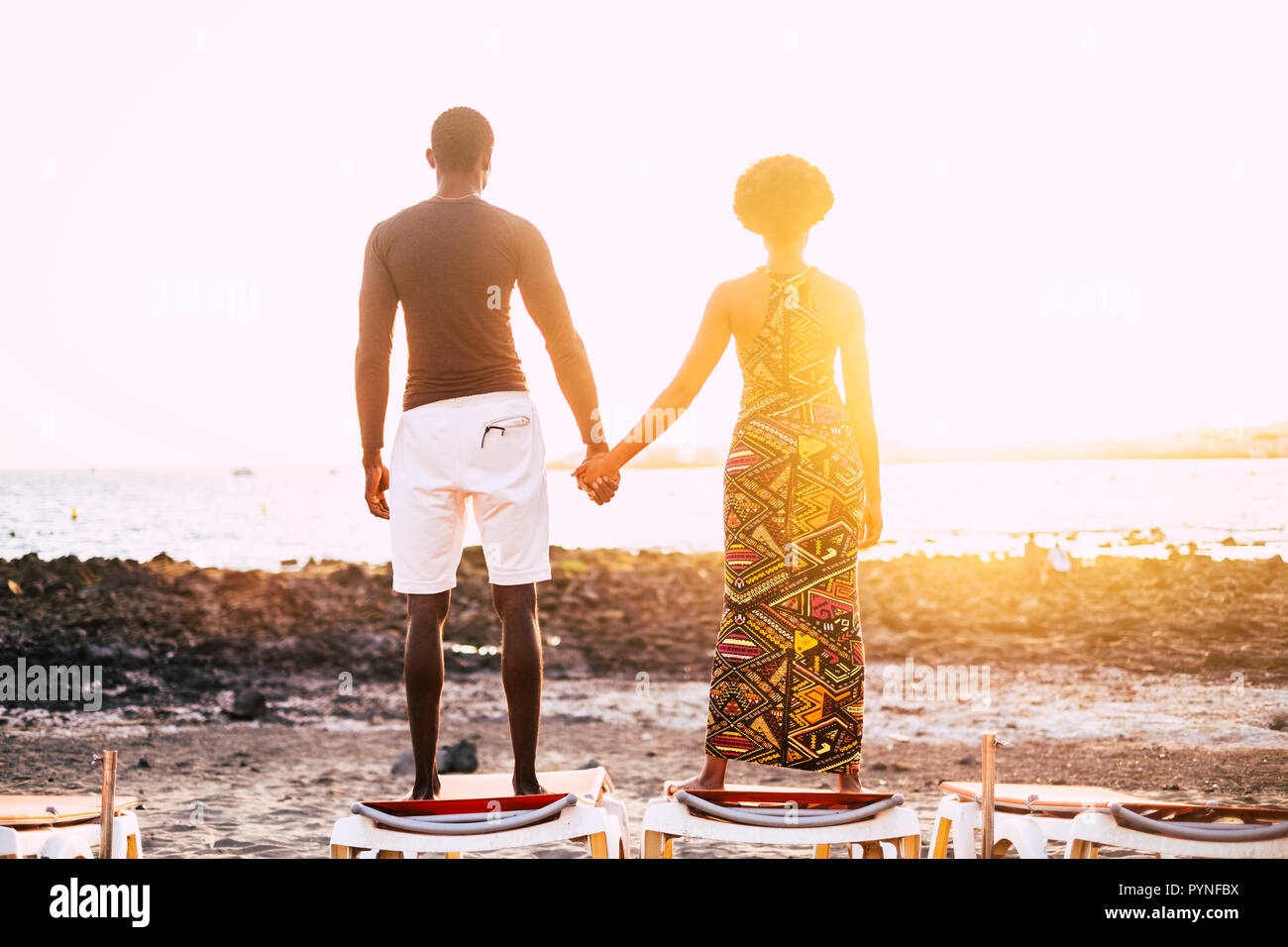 Romantic black couple in love african people looking at the sunset while stand up on a sun beads at the beach in summer holiday or sea lifestyle. Peop Stock Photo