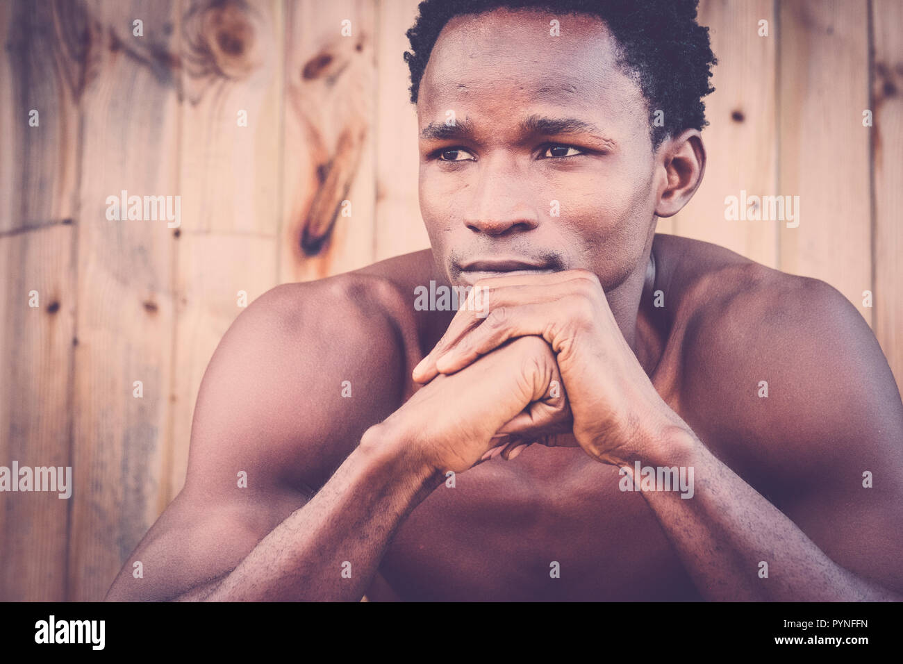 vintage tones retro portrait with black african young man posing in front of the camera. wood background defocused. young boy with thoughts alone. bea Stock Photo