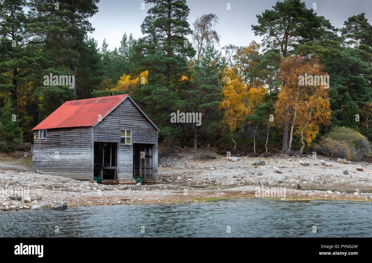 A red-roofed boathouse on the shores of Loch Vaa in the Scottish Highlands, taken during Autumn with the trees showing their bright colours. Stock Photo