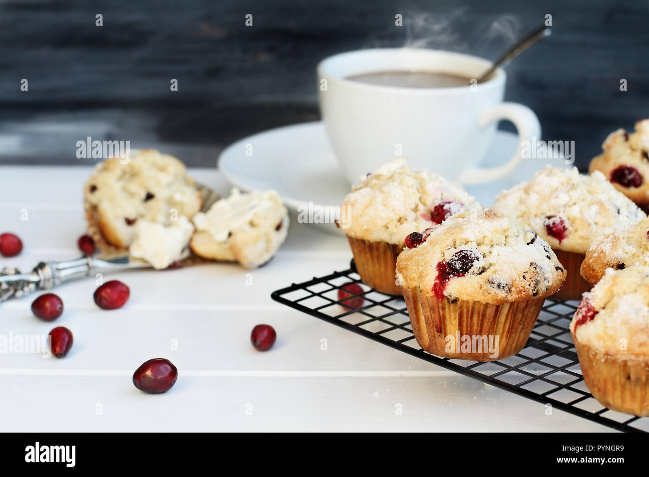 Cranberry Muffins cooling on a bakers rack with extreme shallow depth of field and open muffin with butter and a steaming hot cup of coffee in the bac Stock Photo