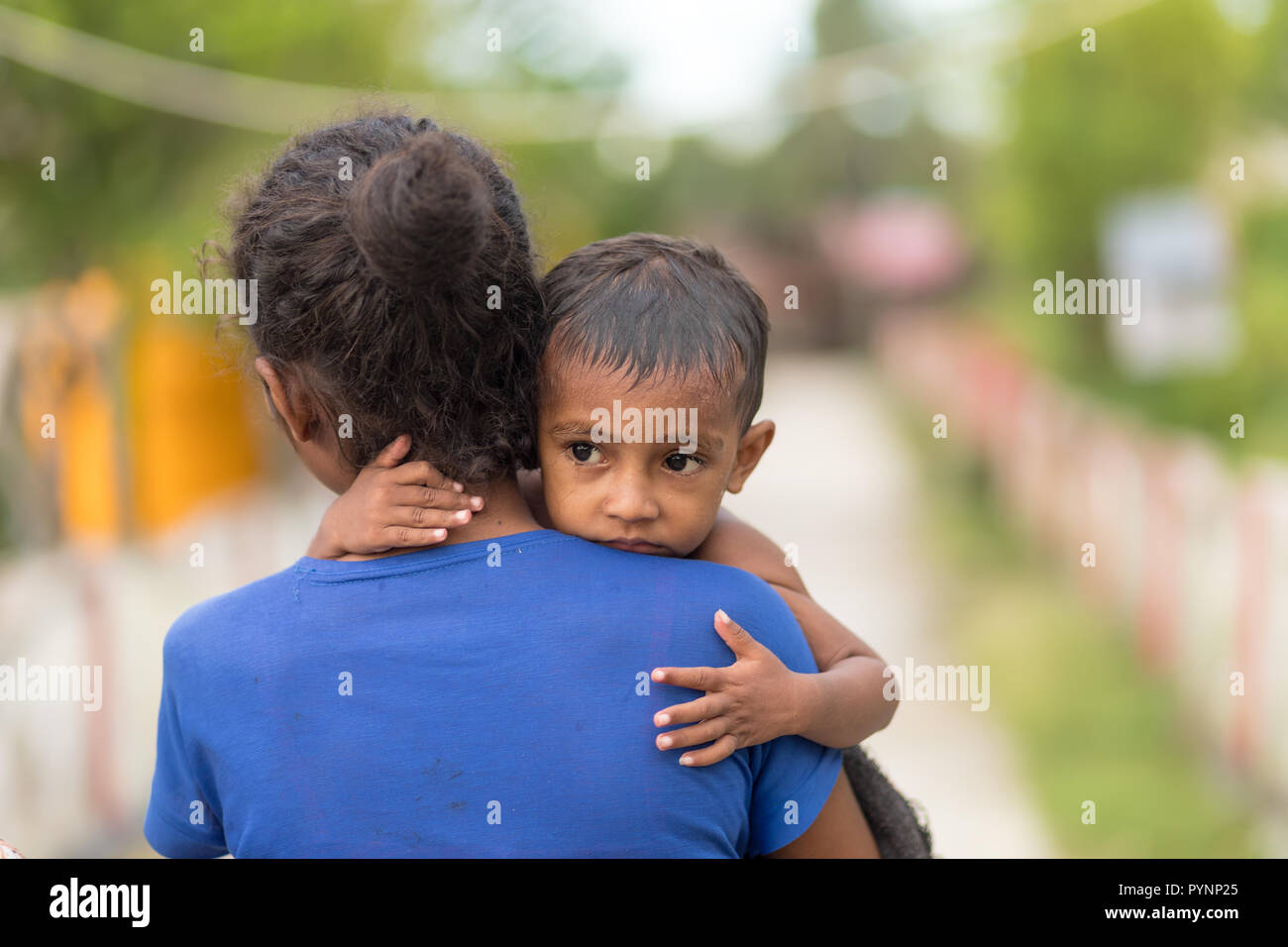 TUNGU VILLAGE, ARU ISLANDS, INDONESIA, DECEMBER 04, 2017 : A mother is carrying her little boy in the street of the Tungu village in the Aru island, I Stock Photo