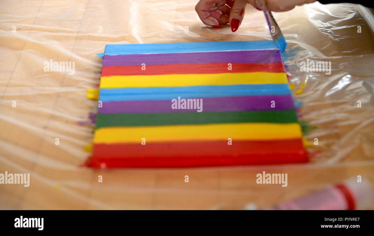 Female artist painting a rainbow with acrylic colors on canvas, hoe made art, DIY tutorial, colorful Stock Photo