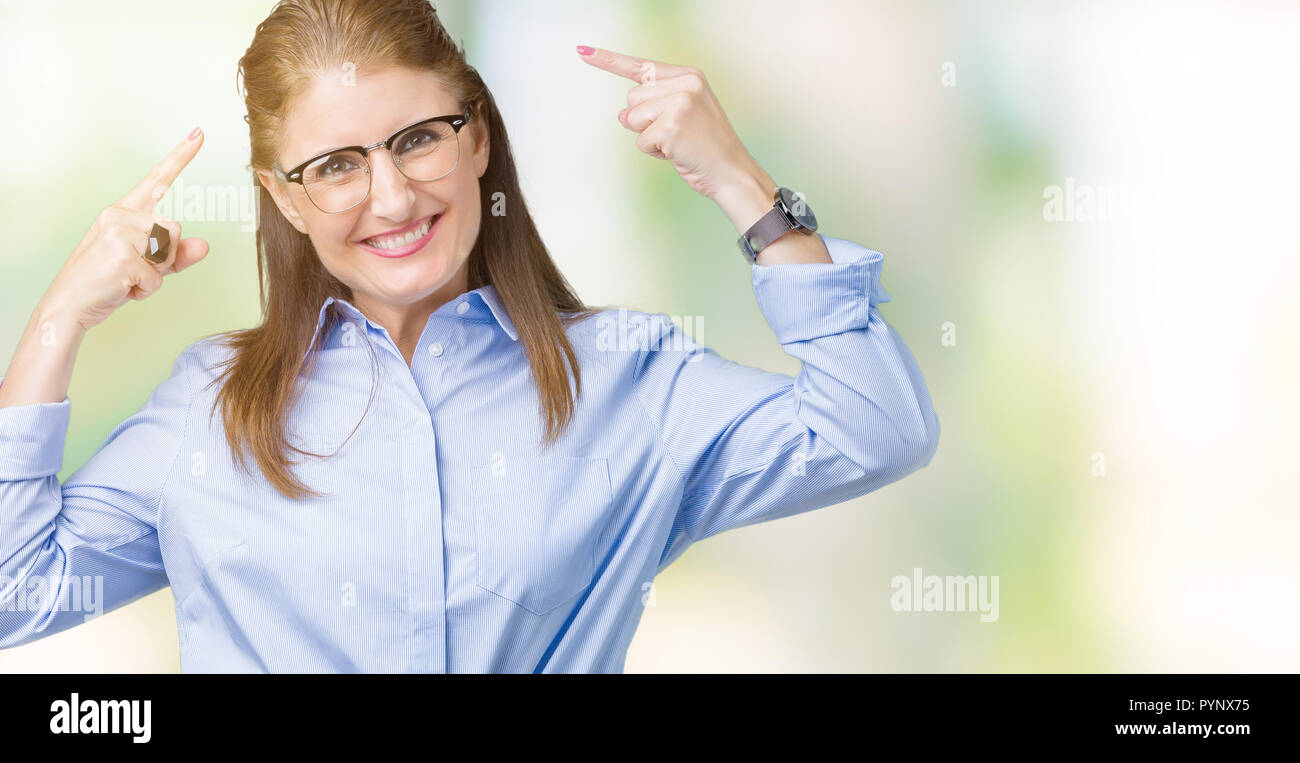 Beautiful middle age mature business woman wearing glasses over isolated background Smiling pointing to head with both hands finger, great idea or tho Stock Photo