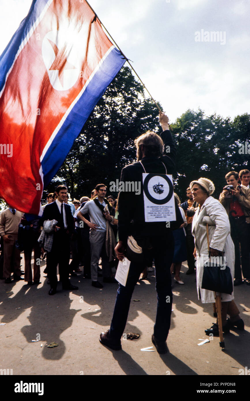 20th annivarsery of the Korean war and a lone protester stands in Hyde Park flying the North Korean flag as well as advertising a photographic exhibition about the subject while an elderly lady looks to be questioning him. 1970s Stock Photo