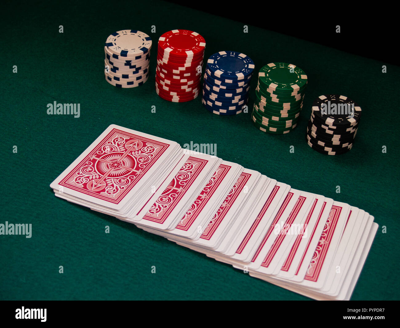A deck of poker cards and poker chips of various colors on a green mat