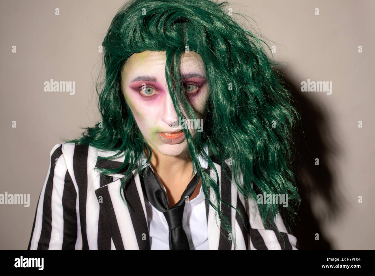 A young woman dresses up for Halloween in a pinstripe suit and green hair. Stock Photo